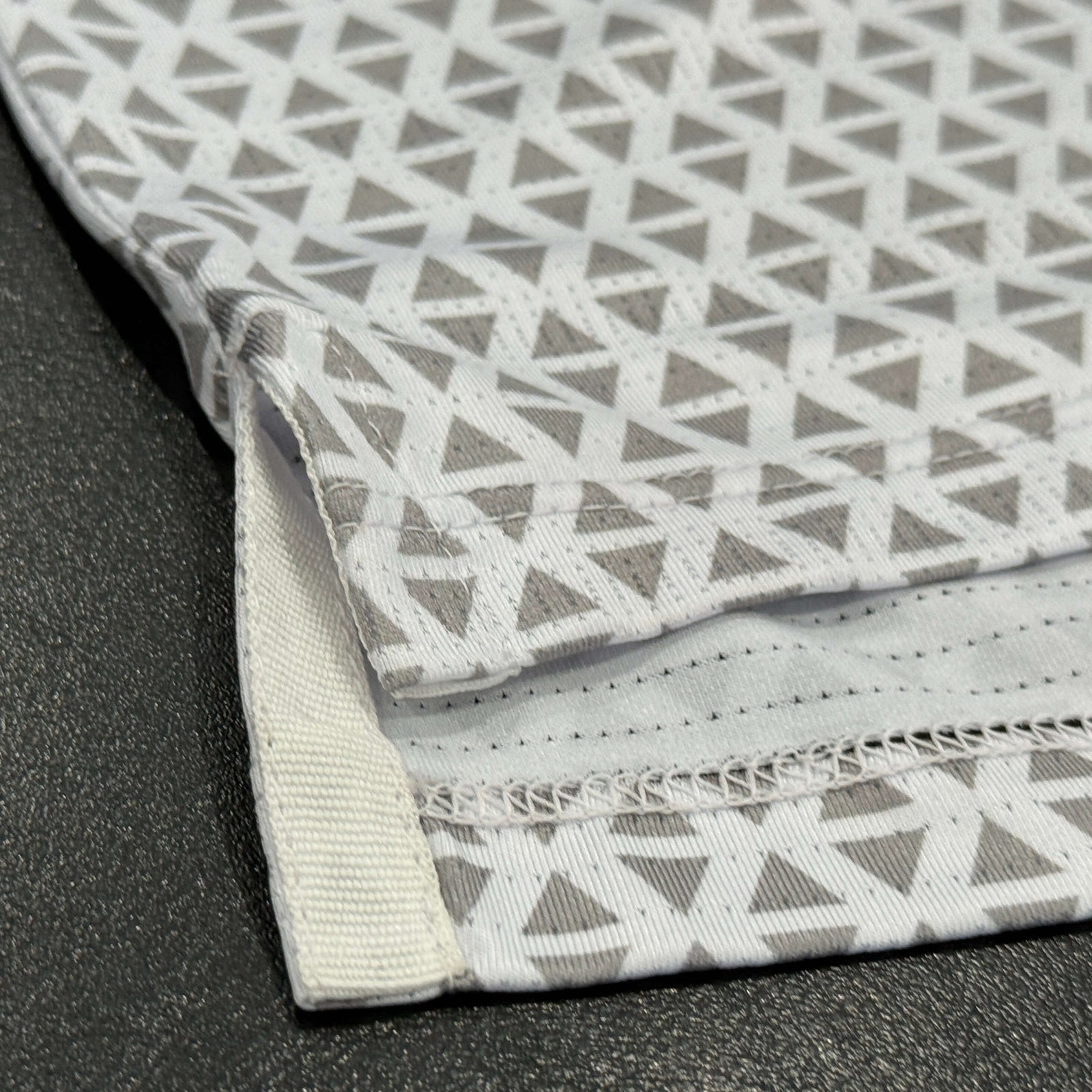Close up of Diamond golf polo in white and grey, featuring the vents on each side of the shirt.