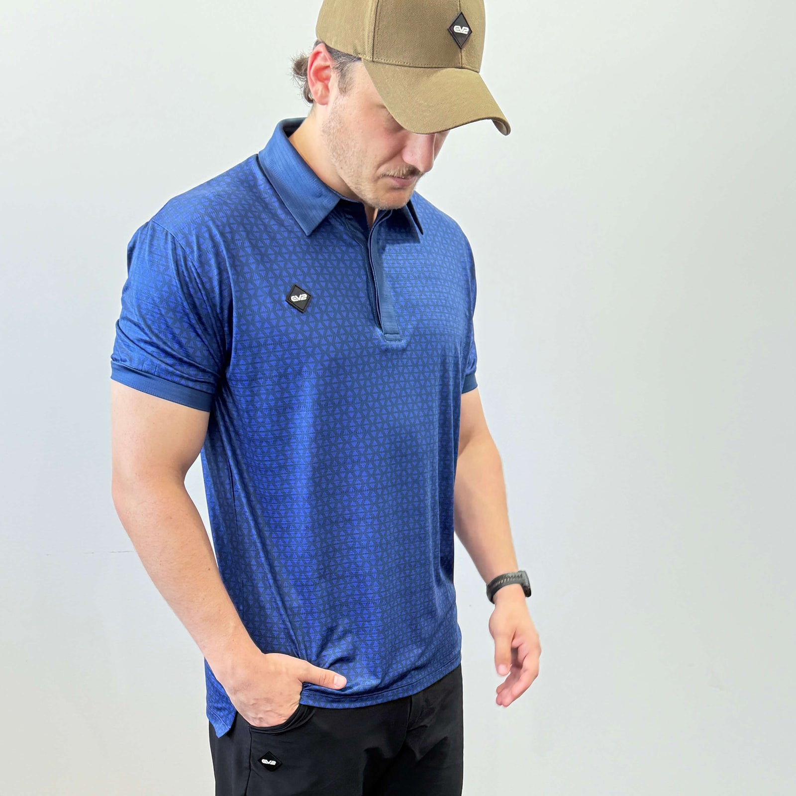 Person wearing a Navy and Blue EV2 Diamond patterned golf shirt and black golf shorts standing in front of a white background.