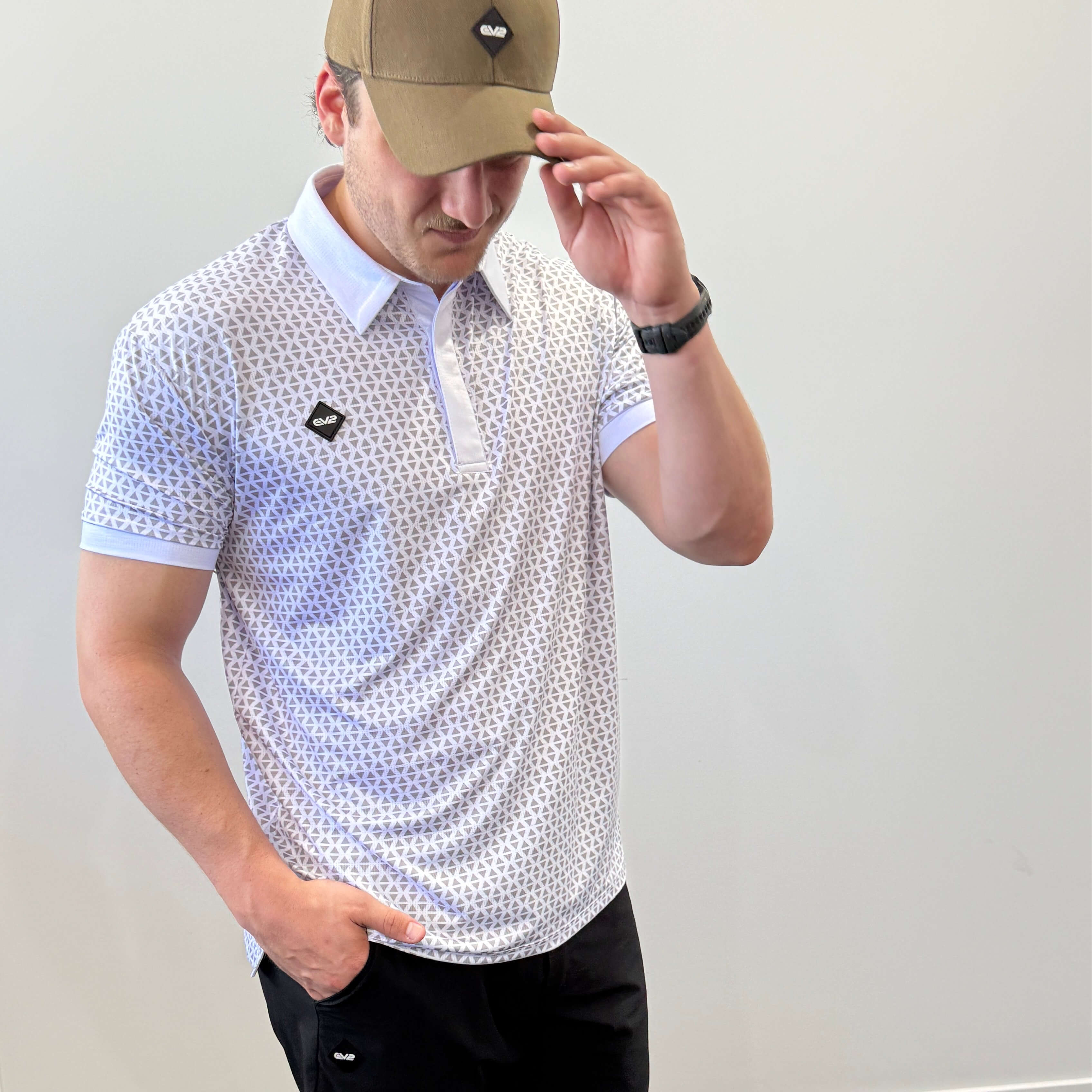 Person wearing a white and grey EV2 Diamond patterned golf shirt and black golf shorts standing in front of a white background.