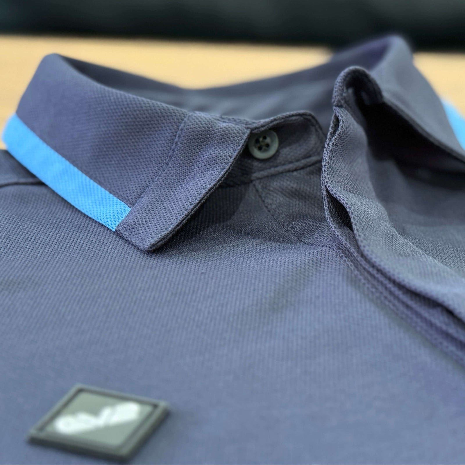 EV2 Fairway Polo in Navy close up of the collar with the black rubber logo in the foreground. 
