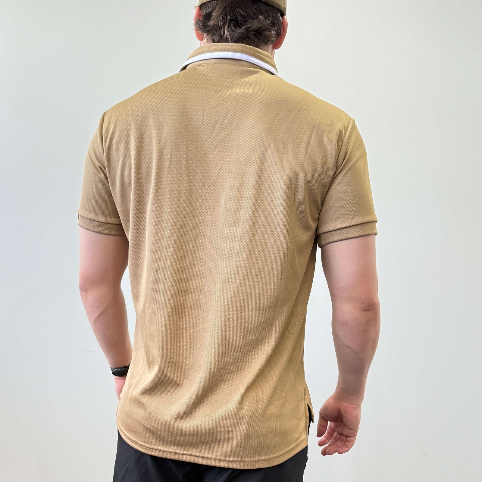 Male model wearing an EV2 Fairway golf polo in Camel seen from the back. The model is wearing black EV2 fairway golf shorts in front of a white background. 