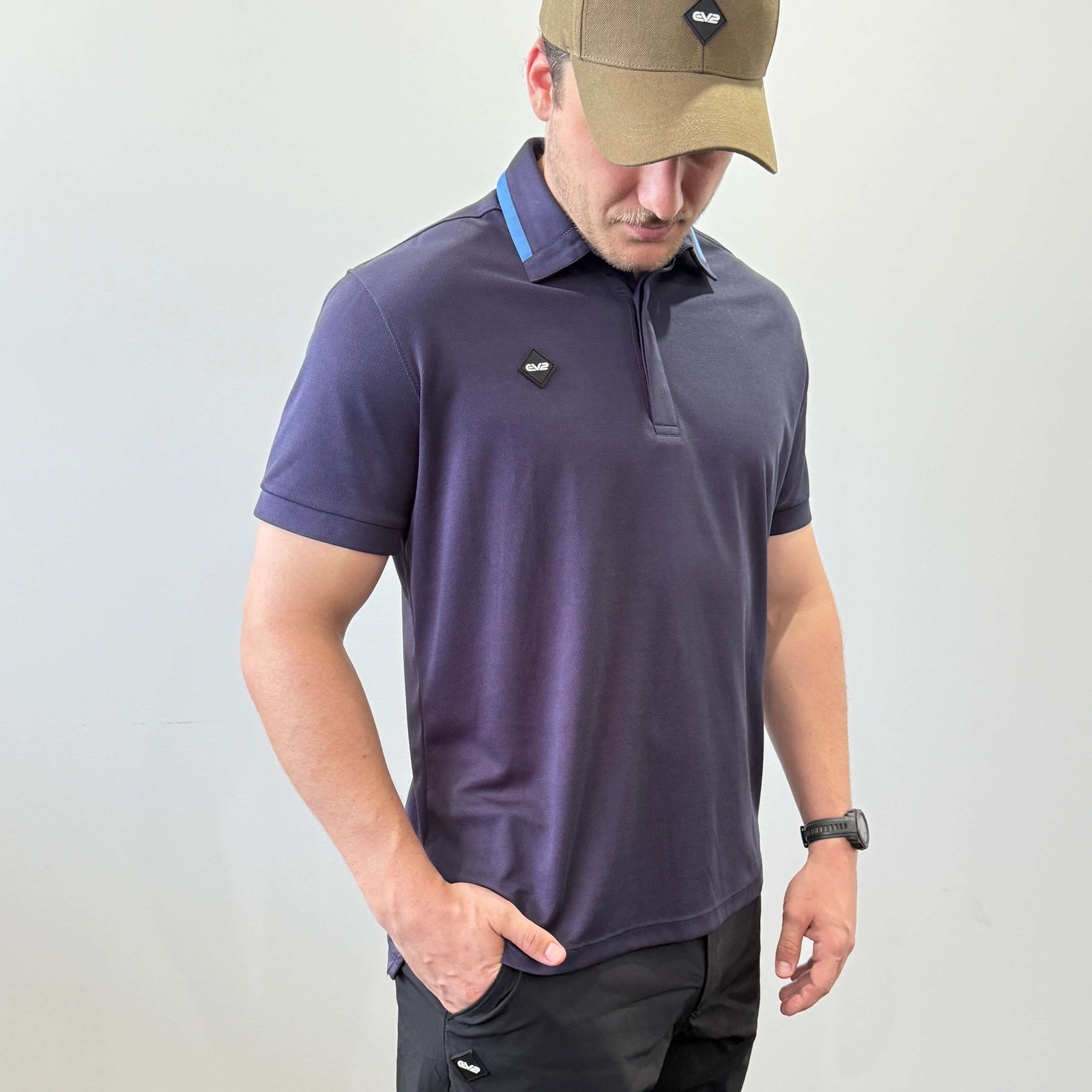 Model wearing EV2 Fairway polo in Navy, chest has a rubber EV2 logo in the shape of a diamond. Model is wearing EV2 Fairway golf shorts in front of a white wall. 