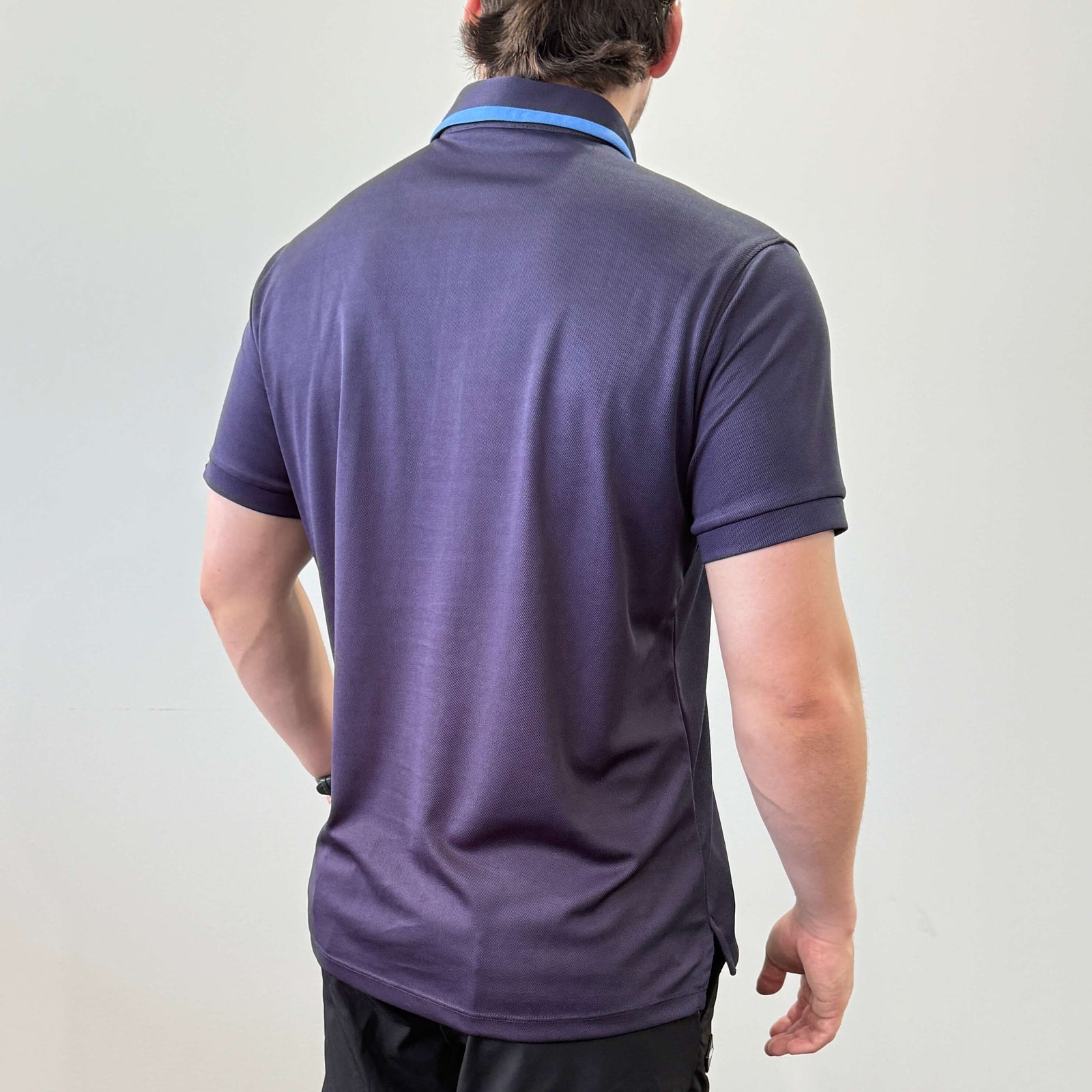 Male model wearing an EV2 Fairway golf polo in Navy seen from the back. The model is wearing black EV2 fairway golf shorts in front of a white background. 