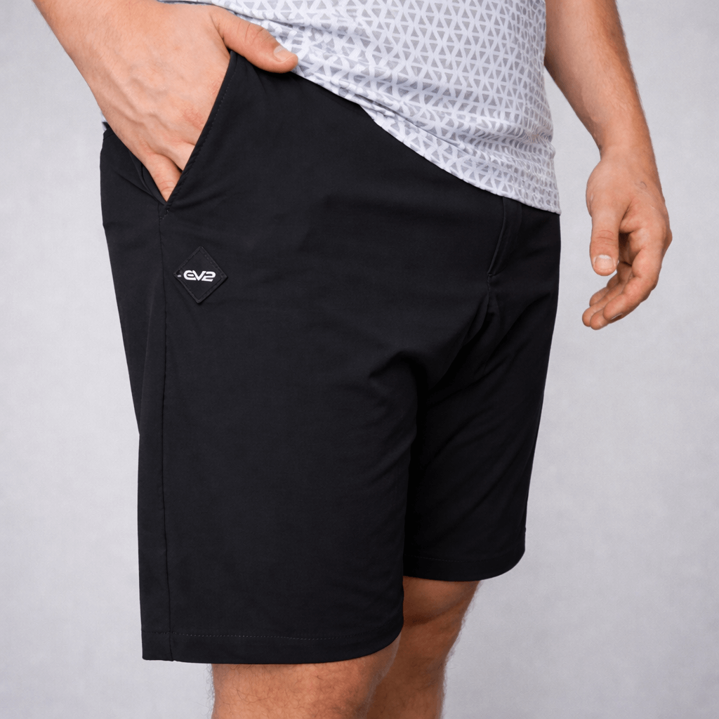 Person wearing black EV2 Fairway shorts with a rubber EV2 logo on a grey studio background