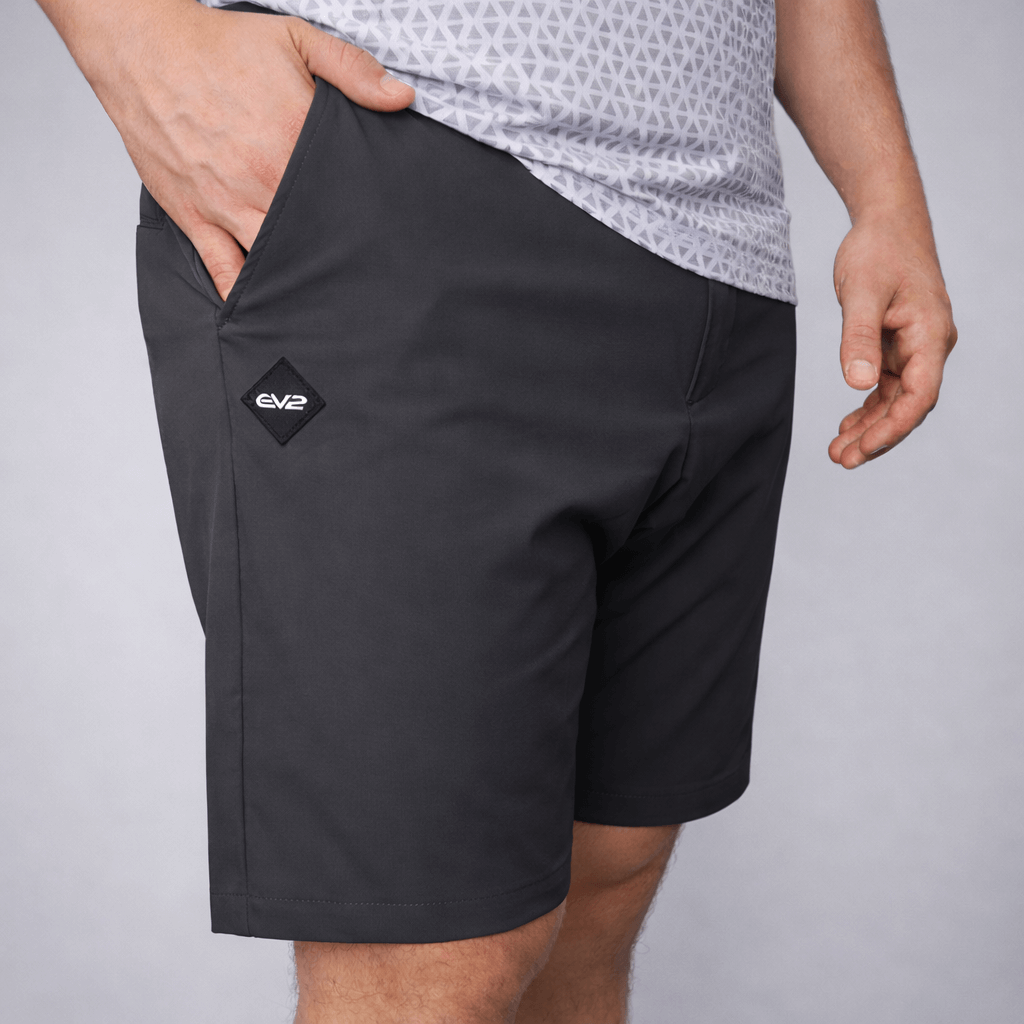 Person wearing black EV2 Fairway shorts with a rubber EV2 logo on a grey studio background