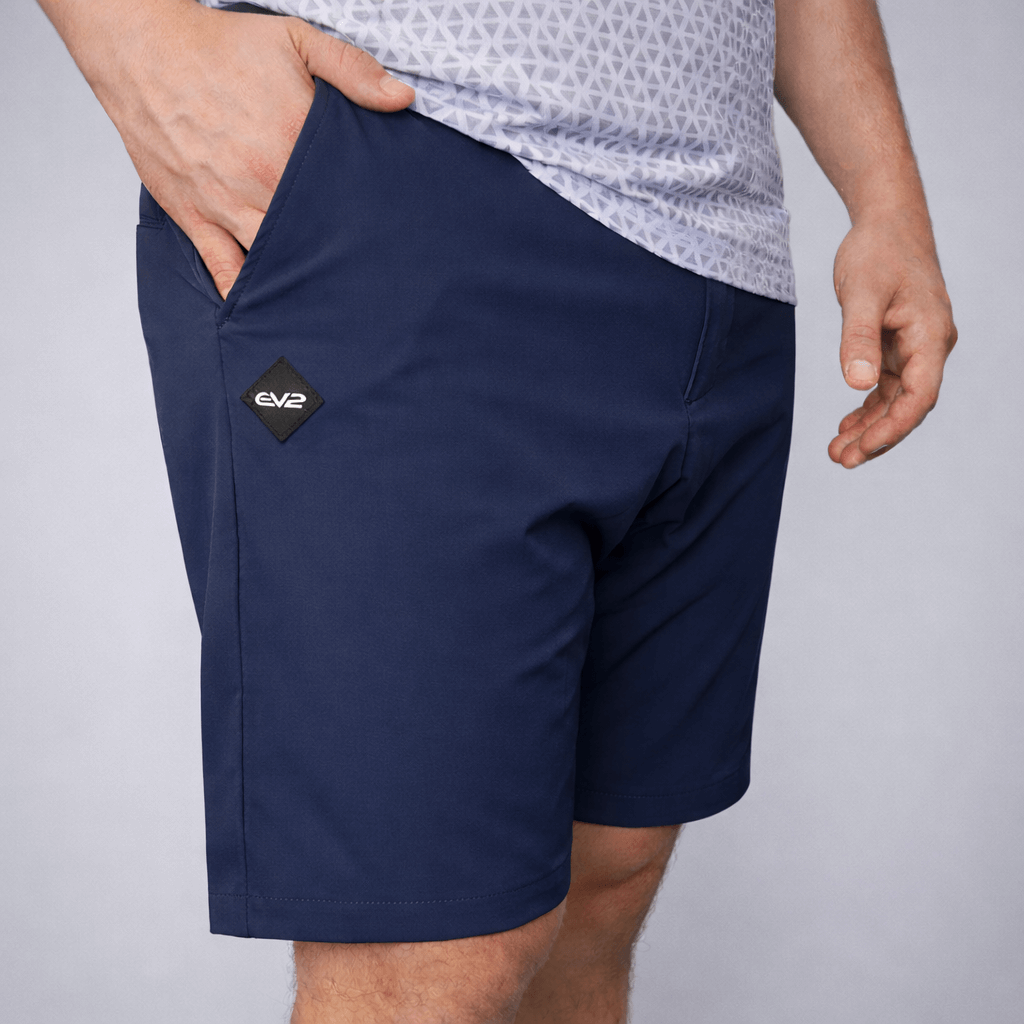 Person wearing Navy EV2 Fairway shorts with a rubber EV2 logo on a grey studio background