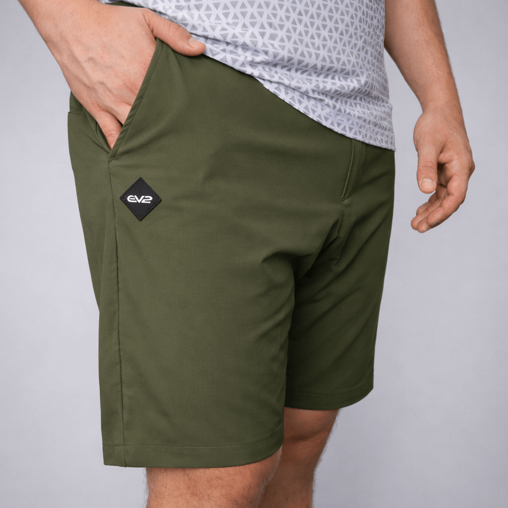 Person wearing Olive EV2 Fairway shorts with a rubber EV2 logo on a grey studio background