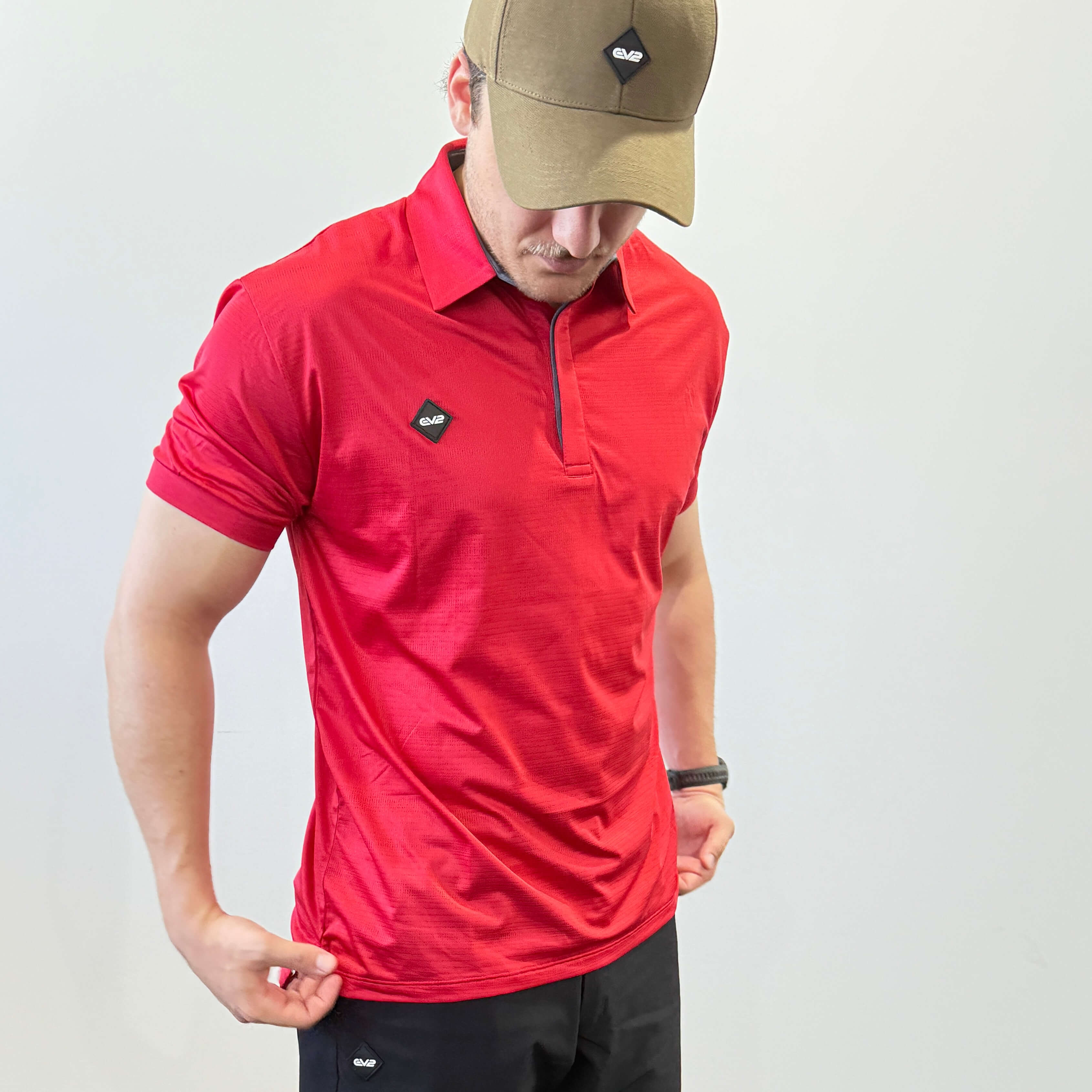 EV2 Masters Polo in bright red with a black rubber logo in the shape of a diamond. Model is also wearing black EV2 golf shorts.