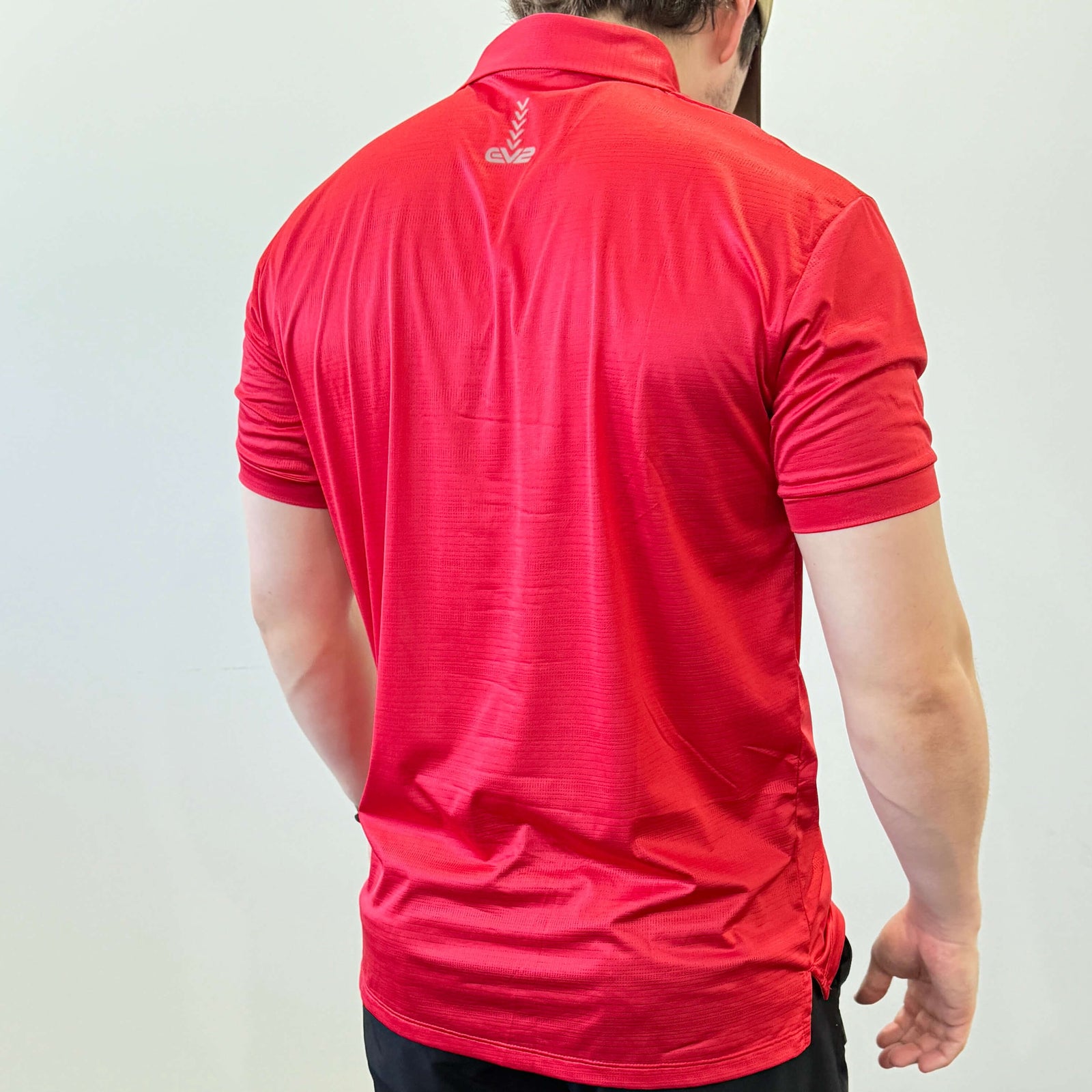 EV2 Masters Polo in bright red with a grey logo along the neck of the shirt. Model is also wearing black EV2 golf shorts.