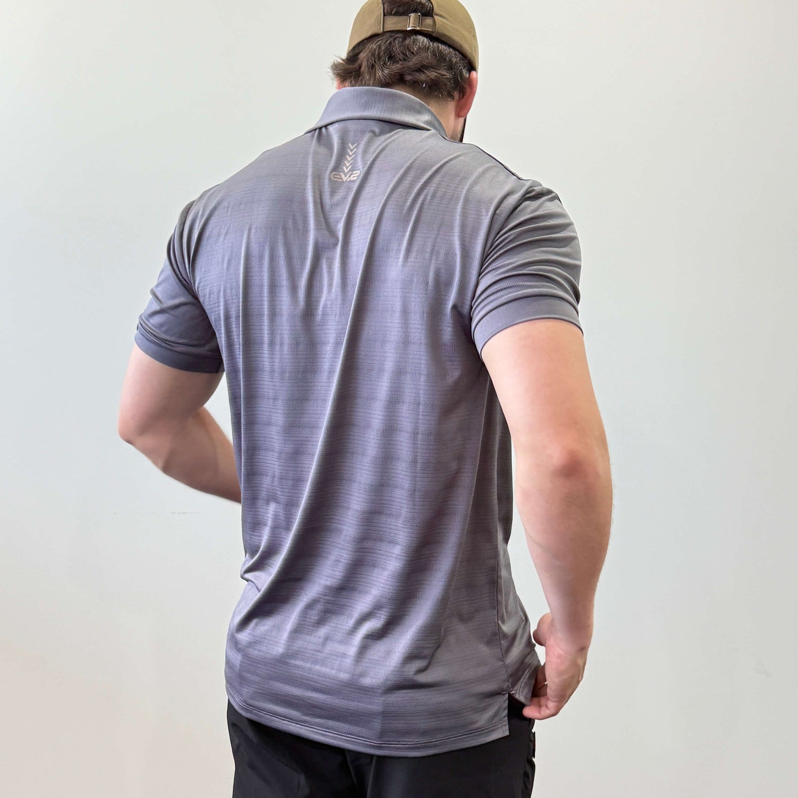 EV2 Masters Polo in Charcoal with a grey logo along the neck of the shirt. Model is also wearing black EV2 golf shorts.