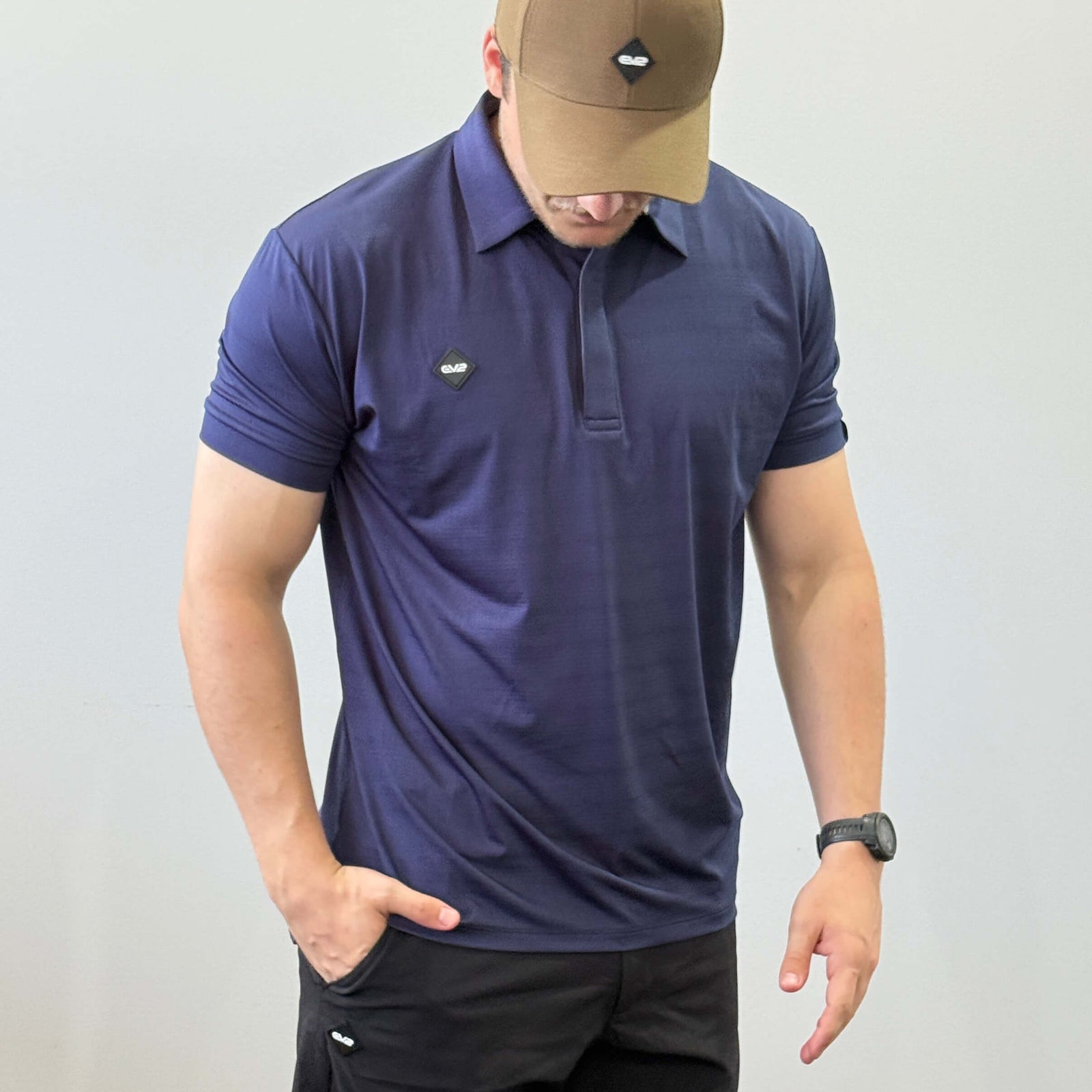 EV2 Masters Polo in Navy with a black rubber logo in the shape of a diamond. Model is also wearing black EV2 golf shorts.