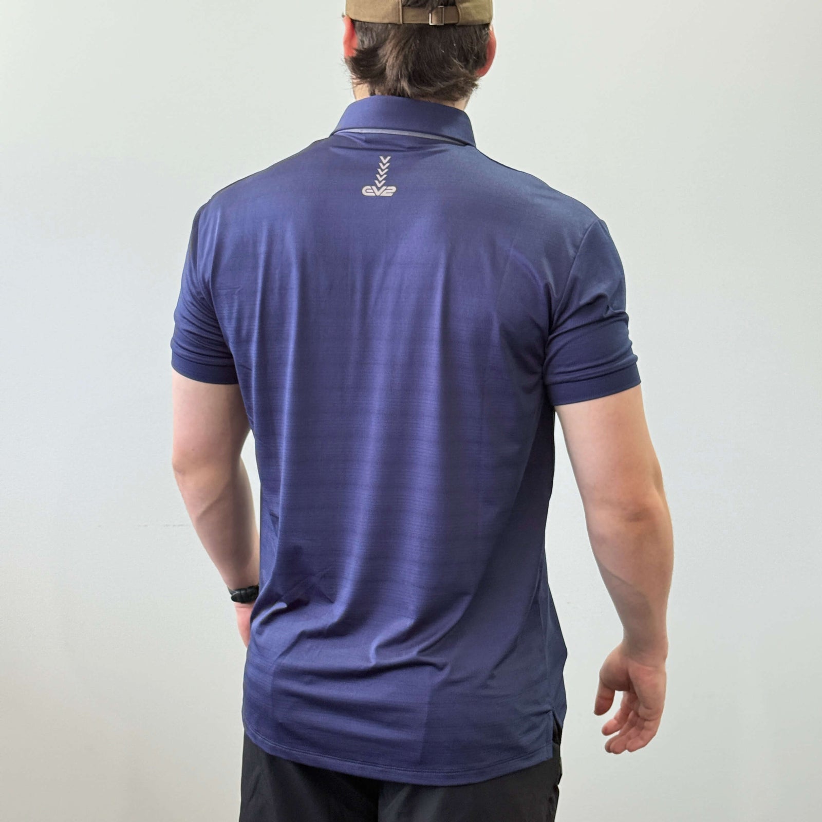 EV2 Masters Polo in navy with a grey logo along the neck of the shirt. Model is also wearing black EV2 golf shorts.